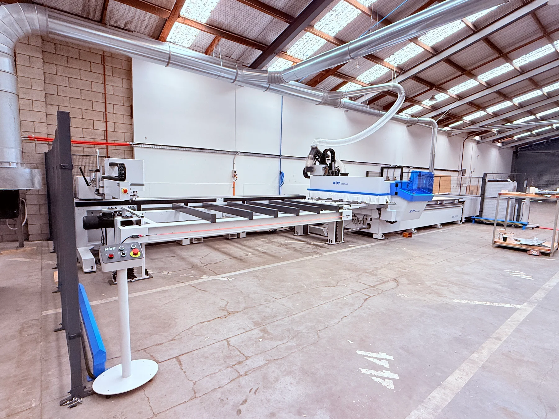 Cabinetry machinery, a loading table and extraction ducts inside the workshop.